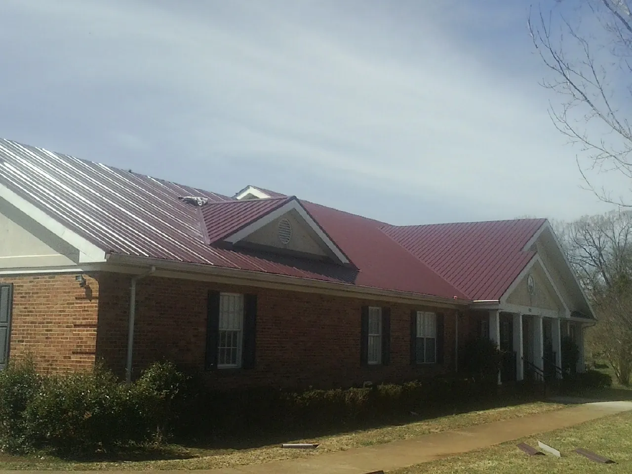Red metal roof with gabled entries on a long brick building, from a Hail Damage Roof Repair job in Falkner