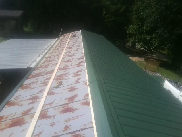 Old rusted panels beside newly installed green metal roofing — Wind Damage Roof Repair by Roofing Brothers in Falkner