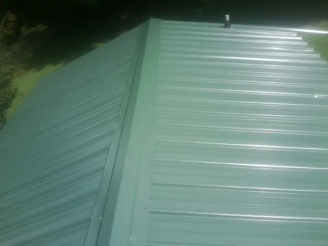 New green metal panels meeting at the ridge of a roof — Flat Roof Repair work by our crew in Falkner