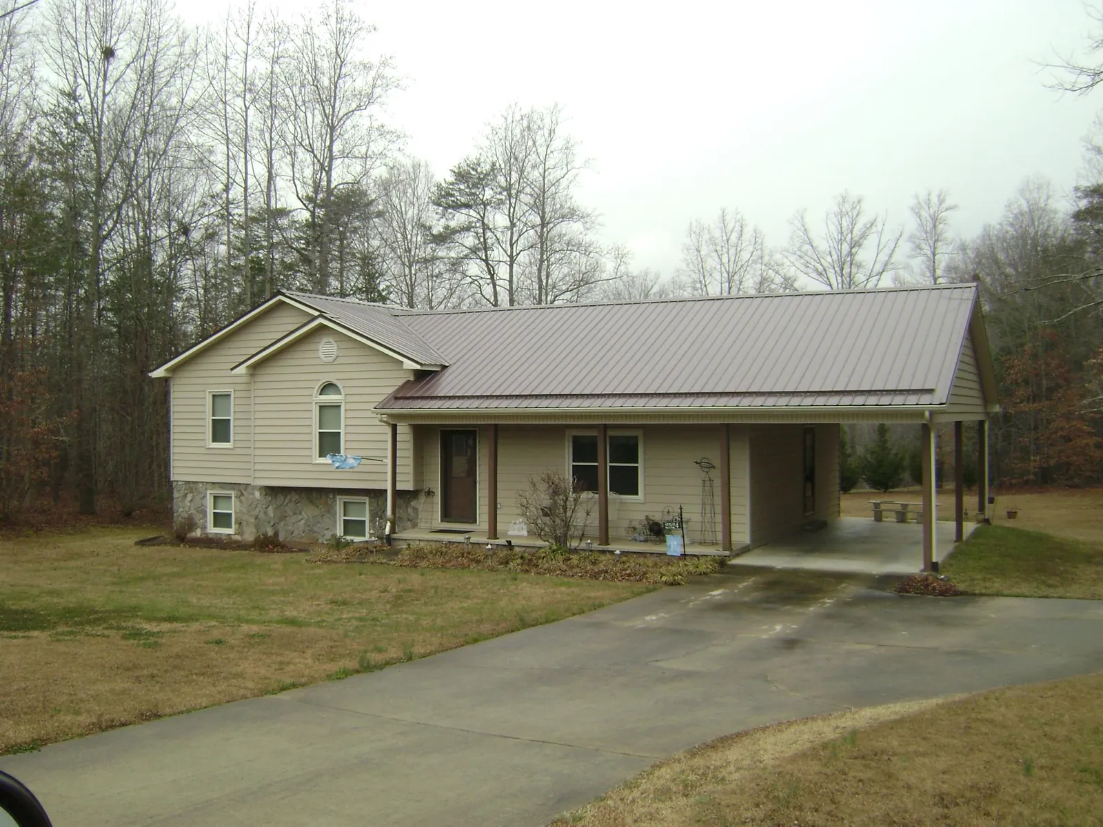 Brown metal roof on a tan split level home with an attached carport in Falkner