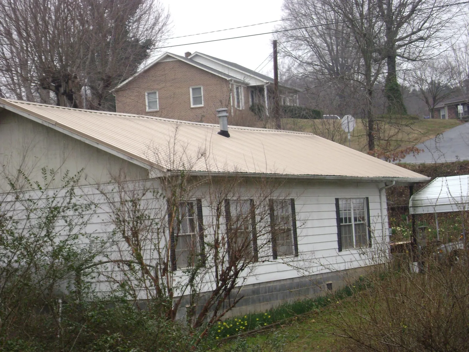 Tan metal roof on a white sided house set into a hillside — Commercial Roofing by Roofing Brothers in Falkner