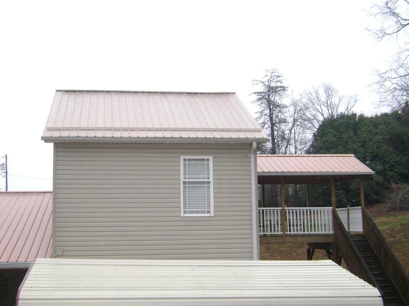 Tan metal roofs on a two story addition and attached porch, from a Roof Replacement job in Falkner